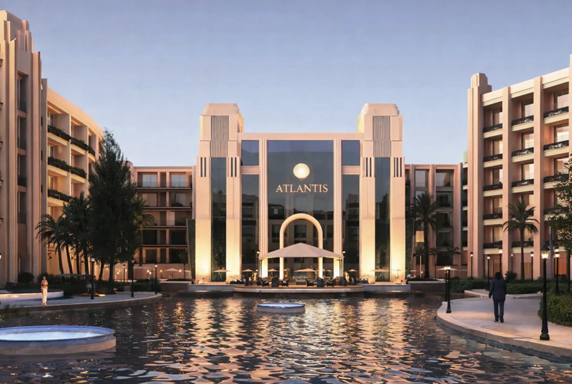 atlantis — developer visualisation — View of Atlantis resort entrance with illuminated beige buildings, palm trees, and a reflecting pool in the foreground at dusk.
