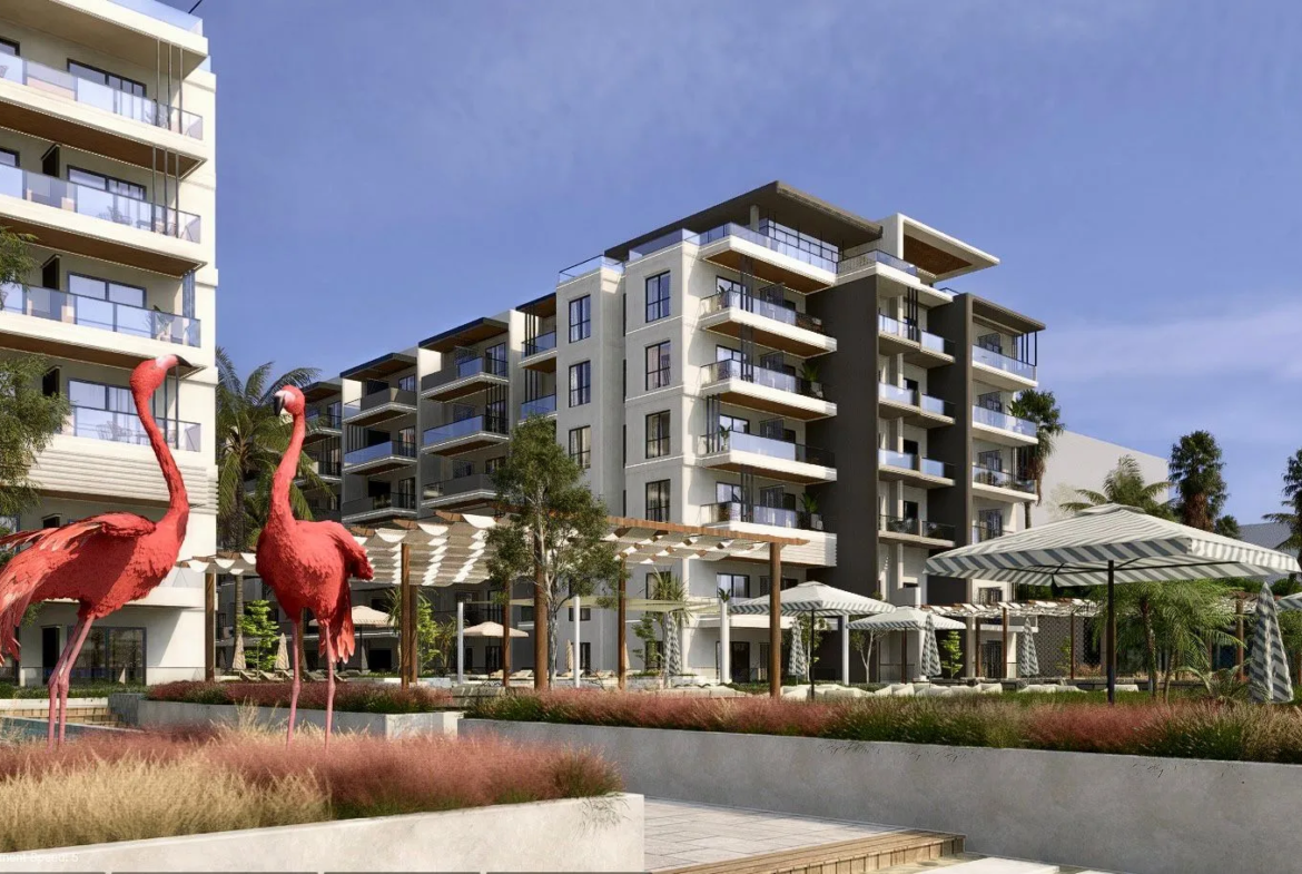 oro — developer visualisation — Modern apartment complex with balconies, outdoor seating areas under striped umbrellas, and two large red flamingo statues in the foreground.