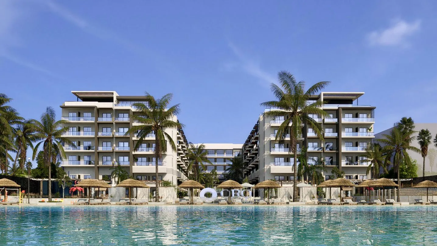 oro — developer visualisation — Modern resort buildings with balconies facing a large turquoise pool, surrounded by palm trees and thatched umbrellas under a clear blue sky.