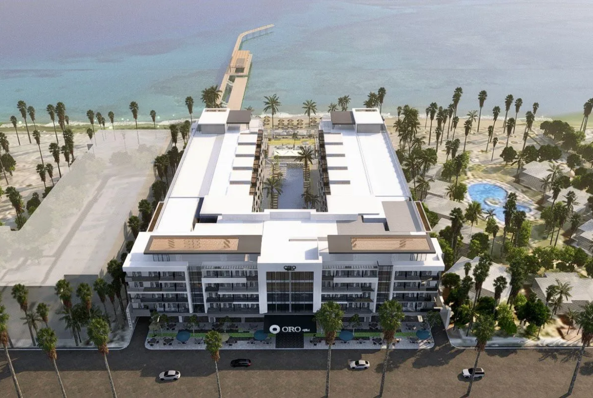 oro — developer visualisation — Aerial view of a modern U-shaped beachfront hotel with a central pool, palm trees, and oceanfront pier.